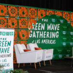 María Antonieta Alcalde Castro, Director, Ipas Latin America and the Caribbean, stands at a podium decorated with "The Green Wave Gathering of Las Americas" text. Beside her are white chairs and a white sofa adorned with green and orange pillows. The backdrop features a vibrant green and orange geometric design, representing the spirit of the Green Wave Gathering.