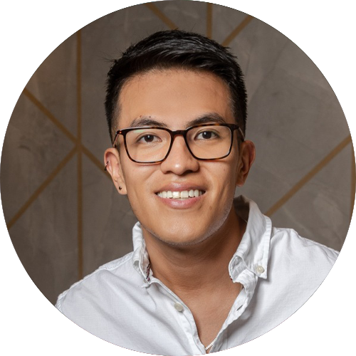 A portrait of David Imbago-Jácome. He has short black hair, is wearing glasses and a white button-up shirt, smiles warmly. The background features a neutral pattern with intersecting lines.