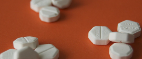 Misoprostol pills image reveals a scattered display of white, hexagonal tablets on an orange surface, some with visible imprints. The tablets are arranged in small clusters, hinting at the presence of multiple individual doses.