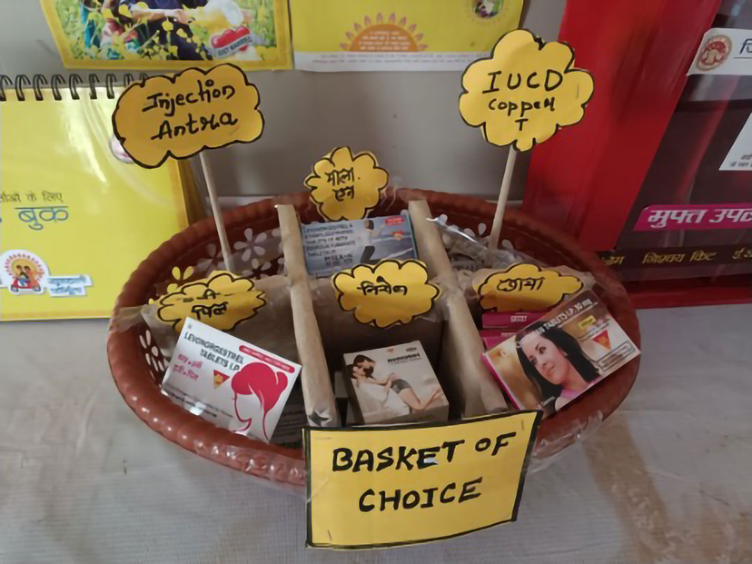 A basket labeled "Basket of Choice" contains various contraceptive options. The basket holds signs for Injection Antira, IUCD copper T, and other contraceptives. Boxes of different contraception methods are organized within the basket.