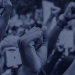 A crowd of people raising their fists in solidarity during a protest. The image is in shades of blue, highlighting the unity and strength of the group.