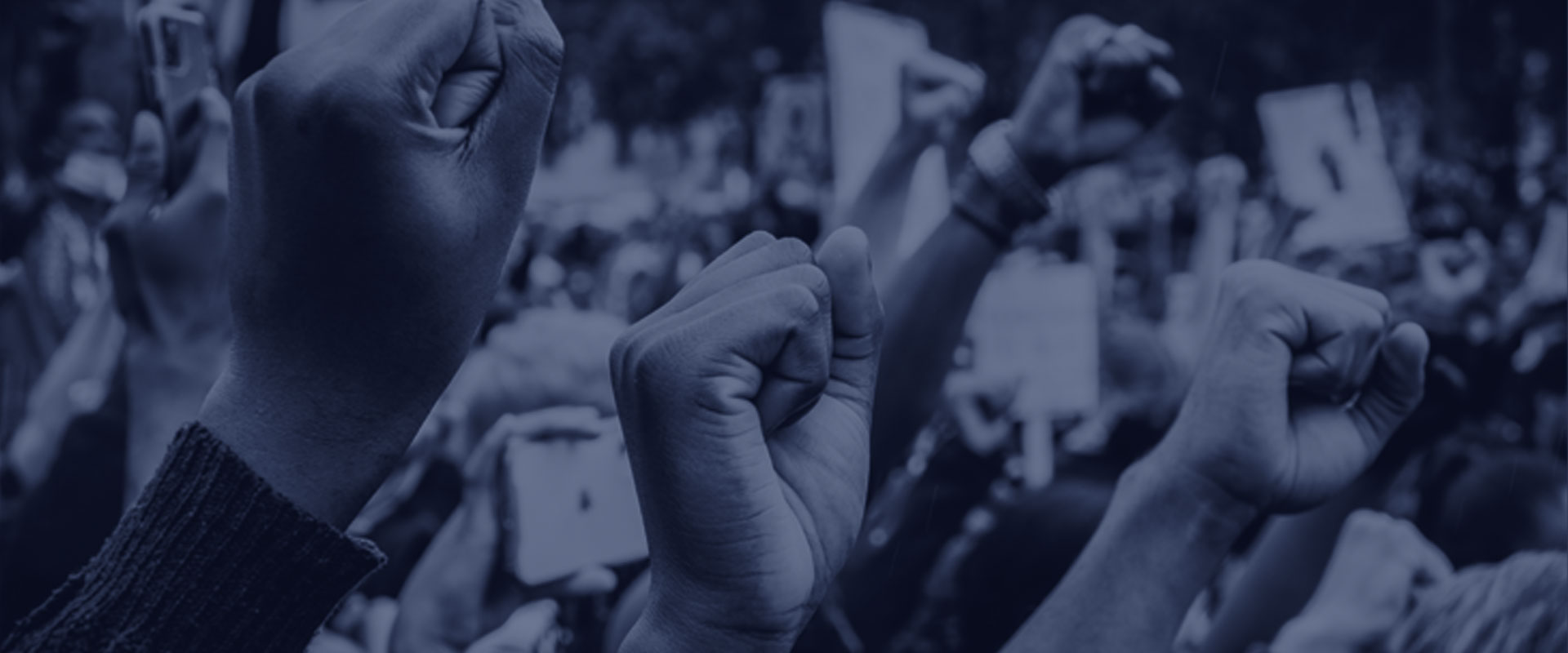 A crowd of people raising their fists in solidarity during a protest. The image is in shades of blue, highlighting the unity and strength of the group.