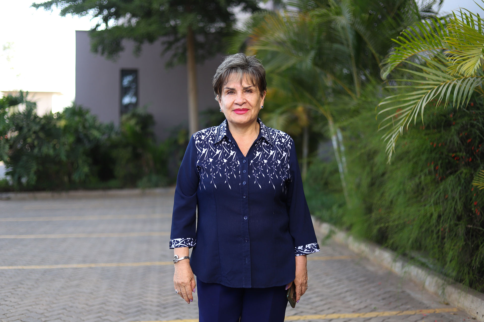 A portrait of Malena Morales standing outside looking at the camera. She is surrounded by greenery and trees. 